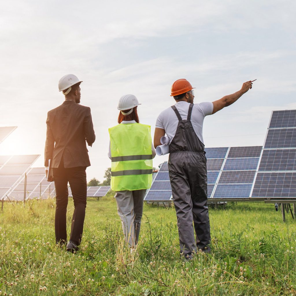 Three engineers in hard hats reviewing a solar array in a field